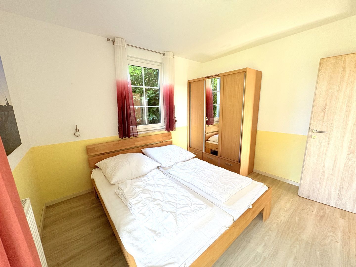 A bedroom with a wooden bed, a wardrobe, and a window with curtains.