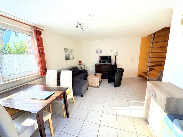 A living room with a dining table, two sofas, a TV, and a staircase.