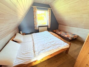 A small, cozy attic bedroom with a sloped ceiling, a single bed, a bench, and a window with floral curtains.