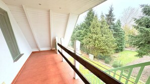 Een balkon met terracotta tegels, witte muren en een groene balustrade.