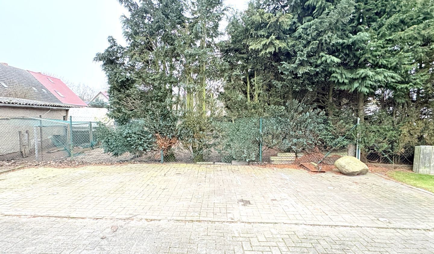 Ein gepflasterter Innenhof mit umzäunter Fläche, Bäumen und einem großen Felsen.