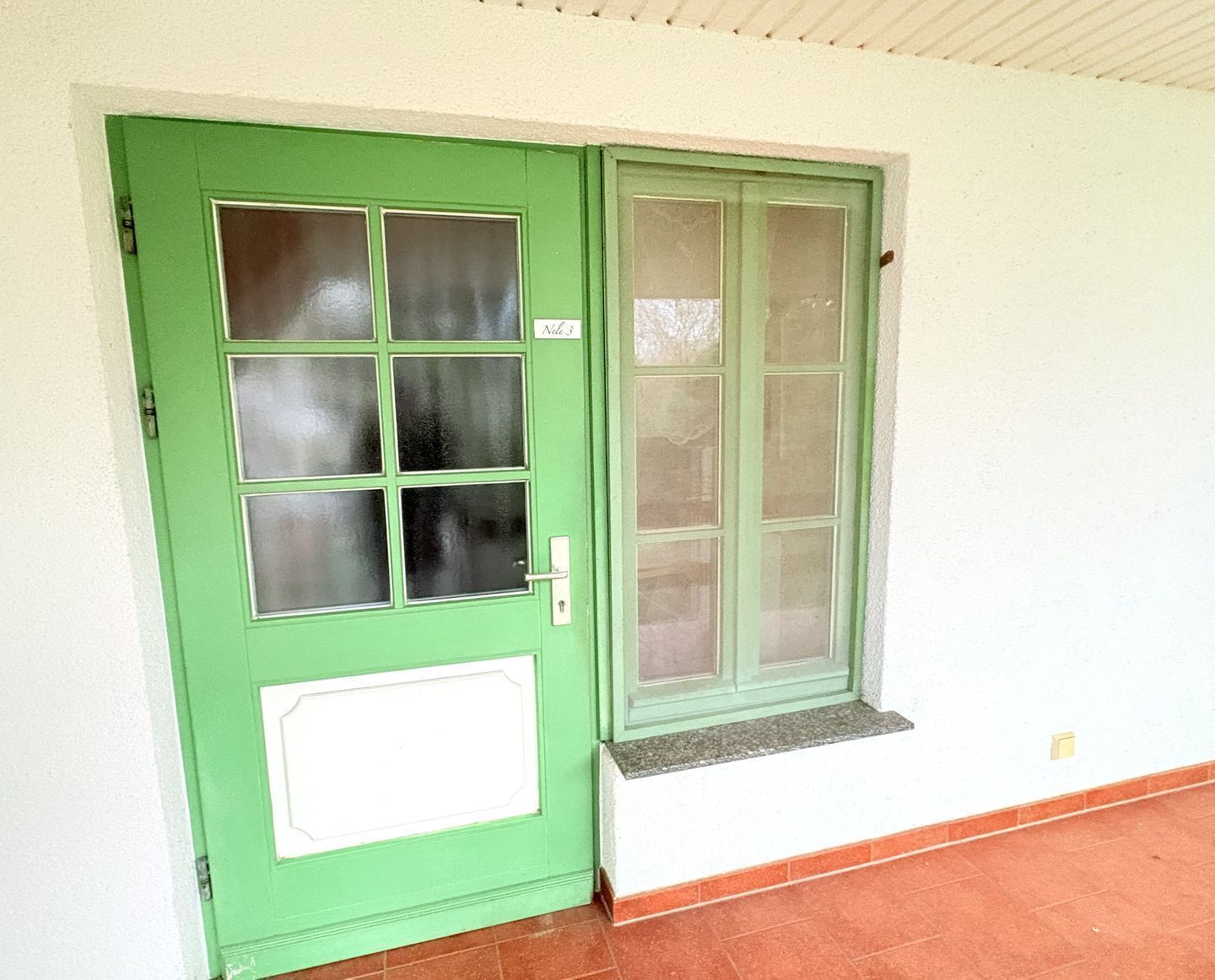 A green door with a window and a white panel, next to a window with a ledge.