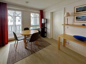 A room with a round table, chairs, a bookshelf, a desk with a bowl, and a window with curtains. - Apartment Having 353 - including use of AHOI bathroom - Accommodation in Seepark Sellin - (Sellin)