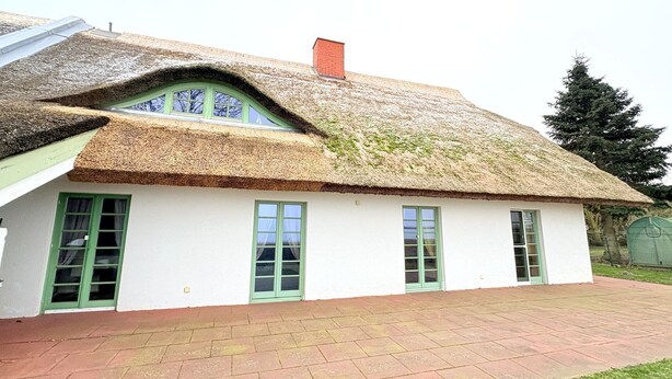 Ein traditionelles Haus mit einem Strohdach, weißer Fassade und grünen Türen und Fenstern.