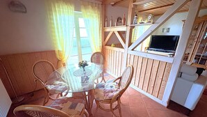 Ein rustikaler Essbereich mit Holztisch und Korbstühle, ein an einer Holzwand montierter Fernseher sowie eine Treppe, die nach oben führt.
