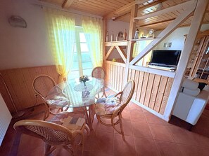 A rustic wooden dining area with a glass table and wicker chairs, a TV mounted on a wooden wall, and a staircase leading upstairs. - Apartment Nele 2 directly on the Bodden with terrace - Terrace apartment for 2 people (Wiek)