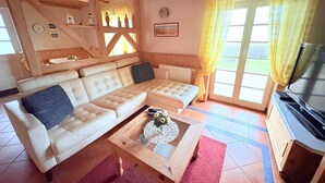 Ein gemütlicher Wohnraum mit einem beigefarbenen Ecksofa, einem Couchtisch aus Holz mit einer Vase und einem Fernseher auf einer Holzkommode.