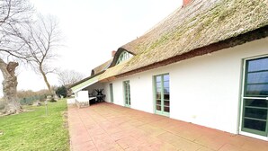 Ein Haus mit einem Strohdach, einer Terrasse mit roten Ziegeln und einer grünen Tür.