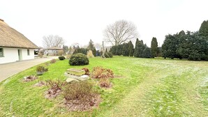 Ein gepflegter Garten mit einem Gebäude mit Strohdach, ordentlich geschnittenen Hecken und verschiedenen Sträuchern.