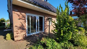A brick house with a large glass door and windows, surrounded by greenery and a clear sky. - Windland Vacation Home—with a garden, fireplace, and sauna—A cozy vacation home (Dranske)