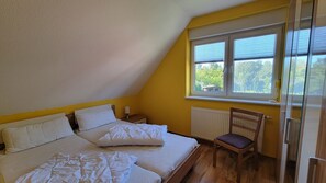 A bedroom with two beds, a window with blinds, a chair, and a radiator. - Windland Vacation Home—with a garden, fireplace, and sauna—A cozy vacation home (Dranske)