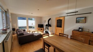 Een woonkamer met een bank, een eettafel en een open haard.