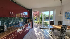 A modern kitchen with red cabinets, a wooden countertop, and a dining area with patterned chairs. - Windland Vacation Home—with a garden, fireplace, and sauna—A cozy vacation home (Dranske)
