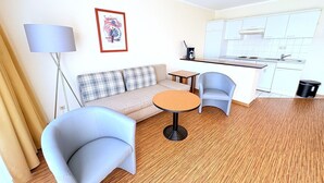 A modern living room with a sofa, two armchairs, a coffee table, a lamp, and a kitchen in the background. - Boddenhof Apartment 46 - ground floor, pet-friendly - Holiday apartment 46 - Helles (Bergen)