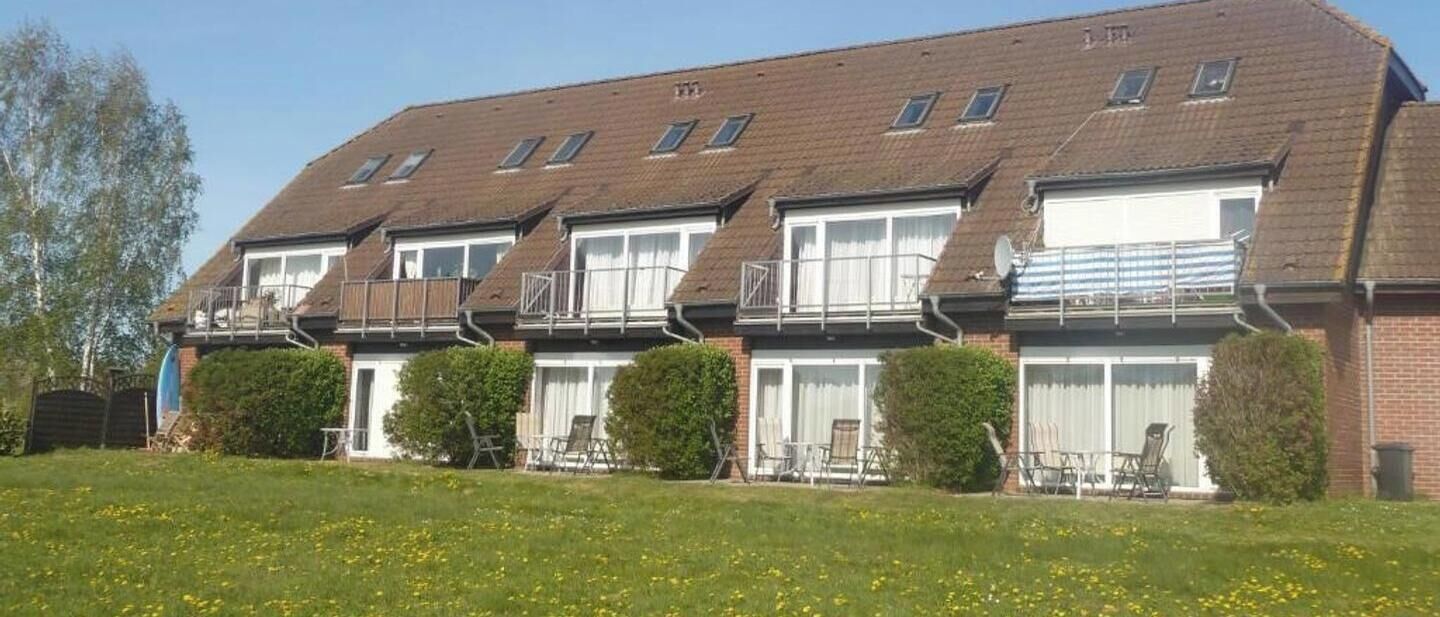 A row of residential buildings with multiple windows, balconies, and a grassy lawn in the foreground.
