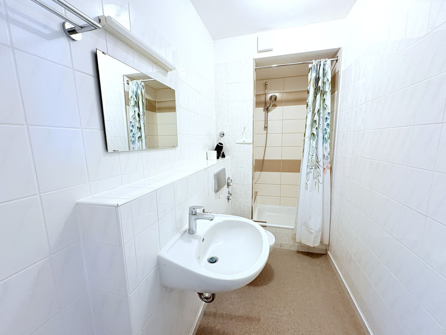 Ein kleines, weißes Badezimmer mit Waschbecken, Spiegel und Dusche.