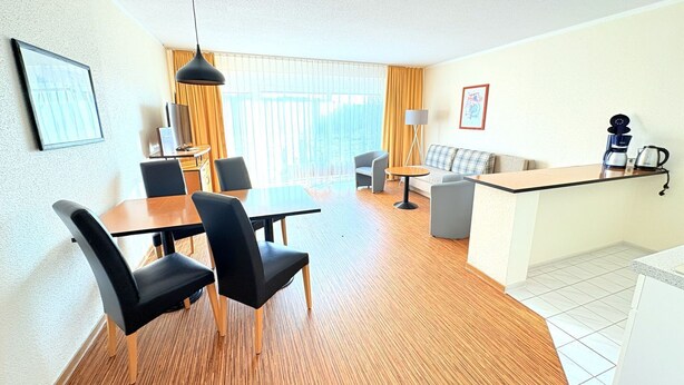 A modern hotel room with a dining area, a sofa, a coffee station, and a large window with curtains. - Boddenhof Apartment 46 - ground floor, pet-friendly - Holiday apartment 46 - Helles (Bergen)