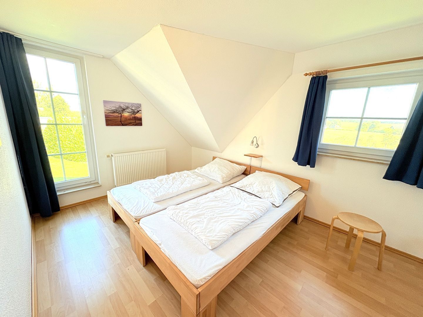 A bedroom with a sloped ceiling, two beds, a small table, and large windows.