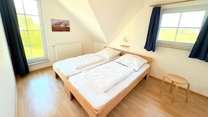 Un dormitorio con techo inclinado, dos camas, una mesita y ventanas amplias.