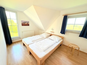 Une chambre avec un plafond en pente, deux lits, une petite table et de grandes fenêtres.