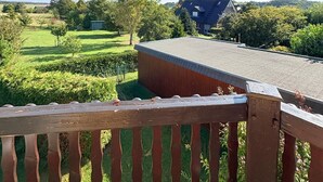 Una terraza de madera con vista a un edificio y un campo verde.