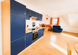 Une cuisine moderne avec des meubles bleus, une table à manger en bois et un canapé bleu dans un salon lumineux doté d’un plafond en pente.