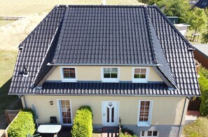 Une maison à deux étages, avec un toit recouvert de tuiles sombres, de nombreuses fenêtres et un petit porche à l’avant.