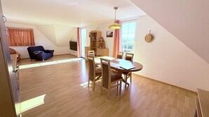 Amplia sala de estar con una mesa de comedor, sillas, un sofá, un televisor y una estantería.