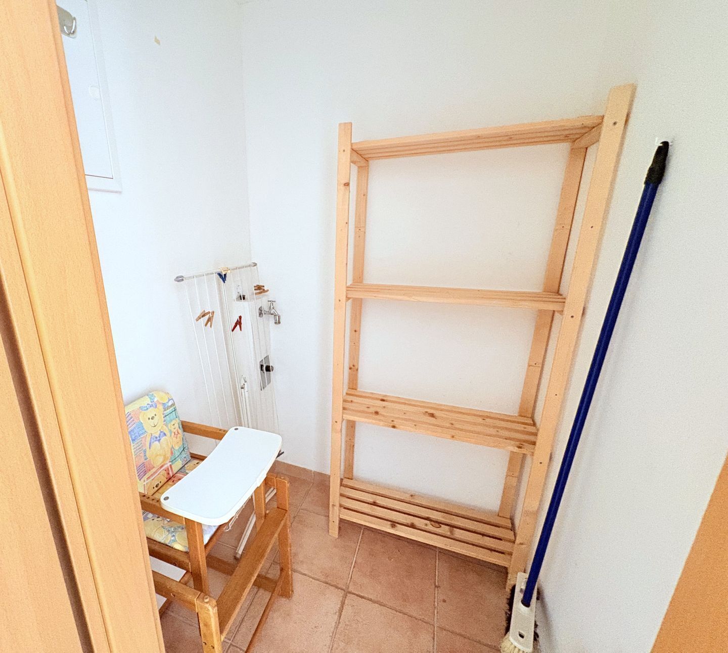Et værelse med en hylde i træ, et hvidt bord og en blå kost.