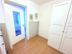 Ein Korridor mit einer Milchglas-Tür, Holzdielenboden und zwei gerahmten Bildern an der Wand.