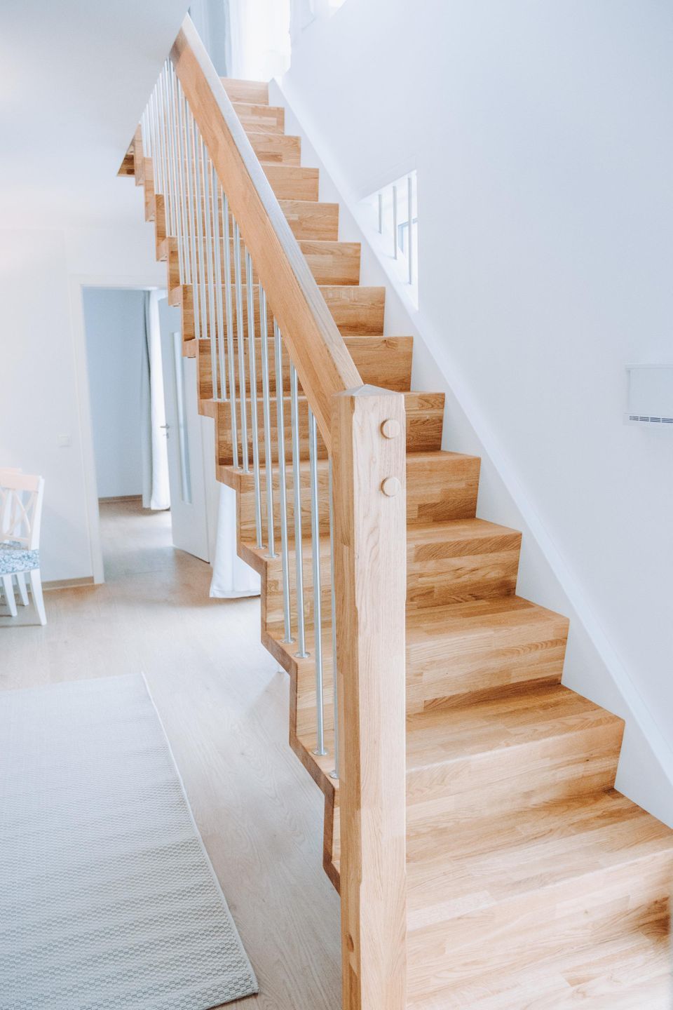 Eine moderne Treppe mit Holzdielen und Metallgeländern, die zu einem Raum mit einer weißen Tür und einem Stuhl führt.