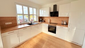 Una cocina moderna con armarios blancos, encimera de madera, campana extractora negra y ventana con vistas al exterior.