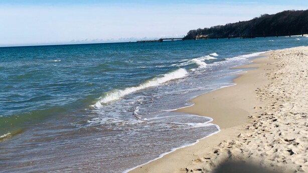 Una playa con agua cristalina, una orilla arenosa y una colina boscosa al fondo.