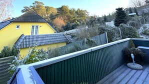 Una casa amarilla con techo de tejas, cerca verde y terraza de madera.