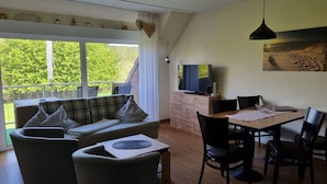 Habitación con sofá, mesa de comedor, sillas, televisor y balcón con vistas a zonas verdes.