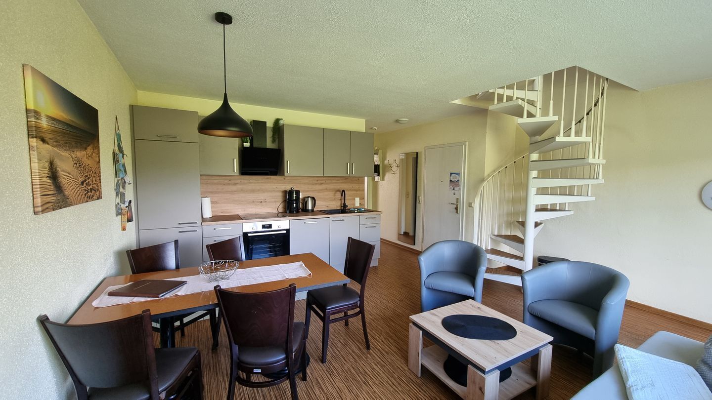 Un espace de vie compact comprenant un coin repas, une cuisine et un escalier en colimaçon.