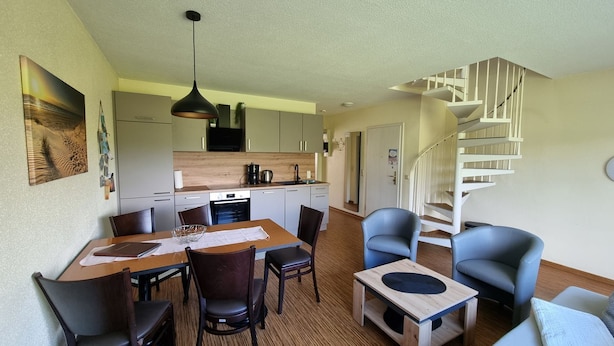 Un espacio habitable compacto con comedor, cocina y una escalera en espiral.