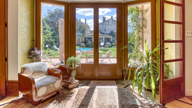 Una habitación con puerta de madera, una silla con cojín, una mesita y una planta en maceta.