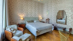 Un dormitorio con una cama grande, dos mesitas de noche, una silla, un espejo y suelo de madera.