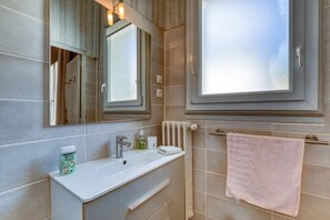 Ein Badezimmer mit weißem Waschbecken, einem Spiegel, einem Handtuchhalter und einem Fenster.