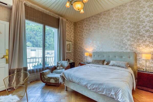 Ein Schlafzimmer mit einem großen Bett, einem Sessel, einer Lampe und einem Fenster mit Vorhängen.