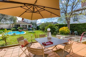 Eine Terrasse im Freien mit Tisch und Stühlen, einem Pool und einem Garten.