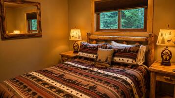 A bedroom with a wooden headboard, a large bed with patterned bedding, two bedside lamps, and a window with blinds.