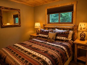 Ein Schlafzimmer mit einem hölzernen Kopfteil, einem großen Bett mit gemusterten Betttextilien, zwei Nachttischlampen und einem Fenster mit Jalousien.