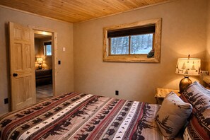 A bedroom with a bed, a window with a view of trees, a lamp, and a door leading to another room.