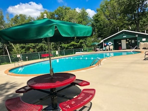 Un espace piscine avec une table et des chaises, un parasol et un bâtiment en arrière-plan.