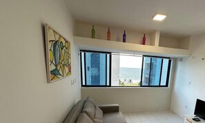 A room with a large window, a sofa, a painting, and a shelf with bottles.