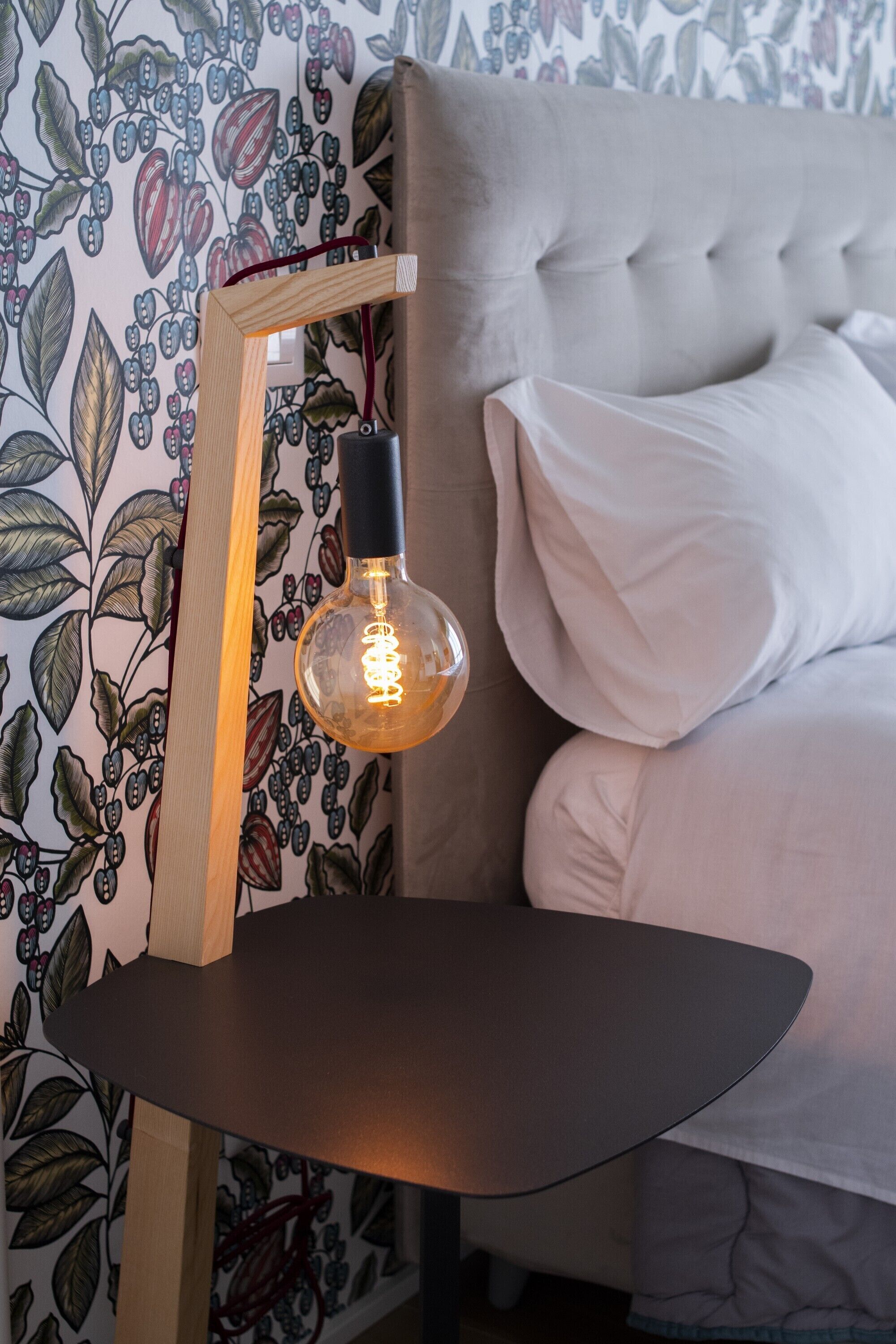 A room with a tufted headboard, a wooden-framed light fixture, and a patterned wallpaper.