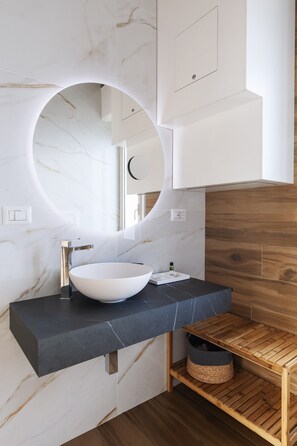 Een moderne badkamer met een wit marmeren wastafel, een ronde spiegel en een houten plank.