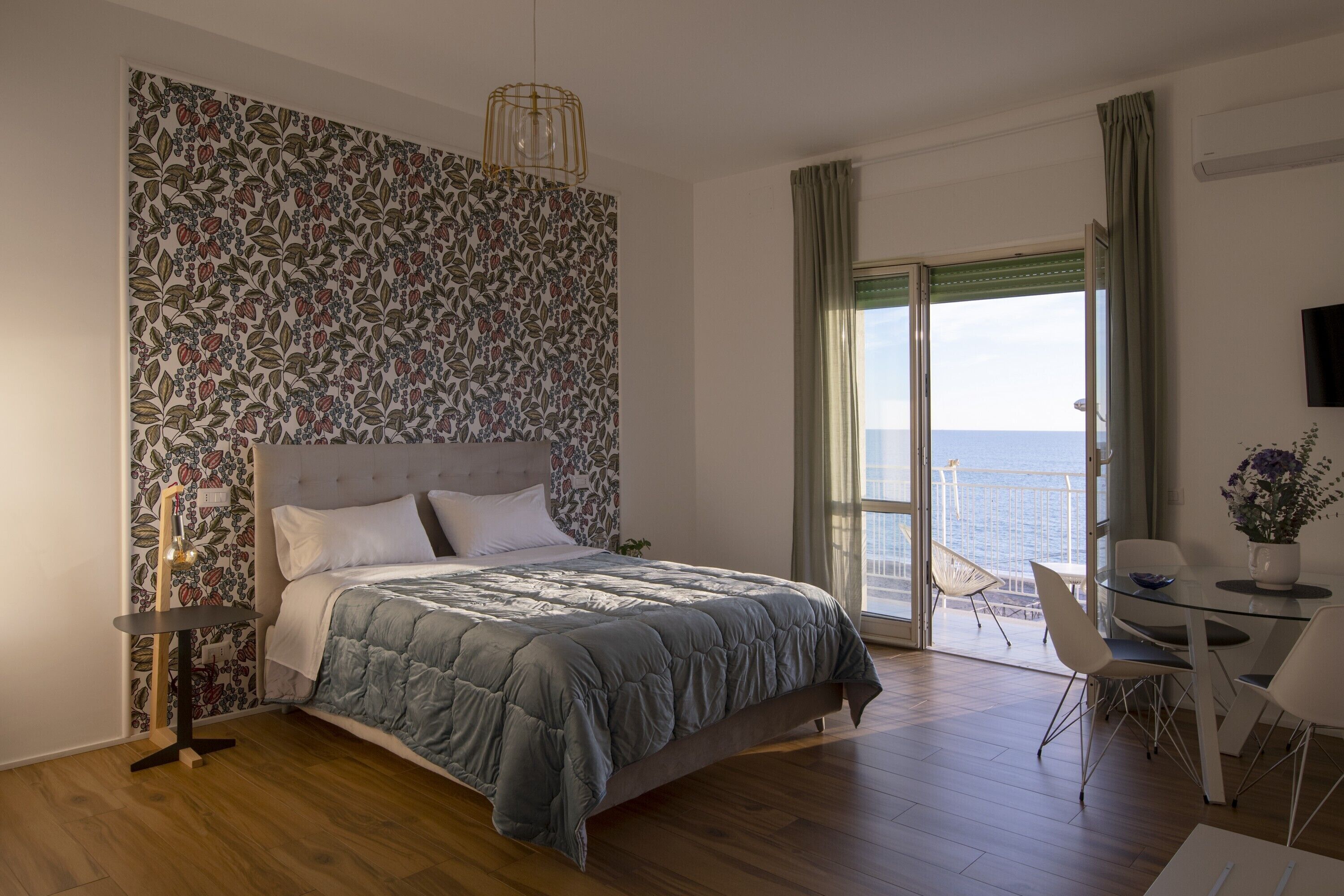 A bedroom with a large bed, a glass table, and a view of the sea.